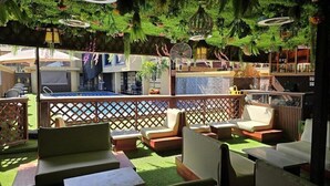 Ein Außenbereich mit Sitzgelegenheiten, gepolsterten Stühlen und Tischen, einem Pool und einer Bar mit Regalen voller Flaschen und einem Ventilator.