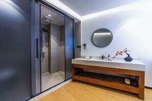 A modern bathroom with a glass shower enclosure, a wooden vanity, a round mirror, and a vase with flowers. - Shangri La cuckoo homestay (Deqin)