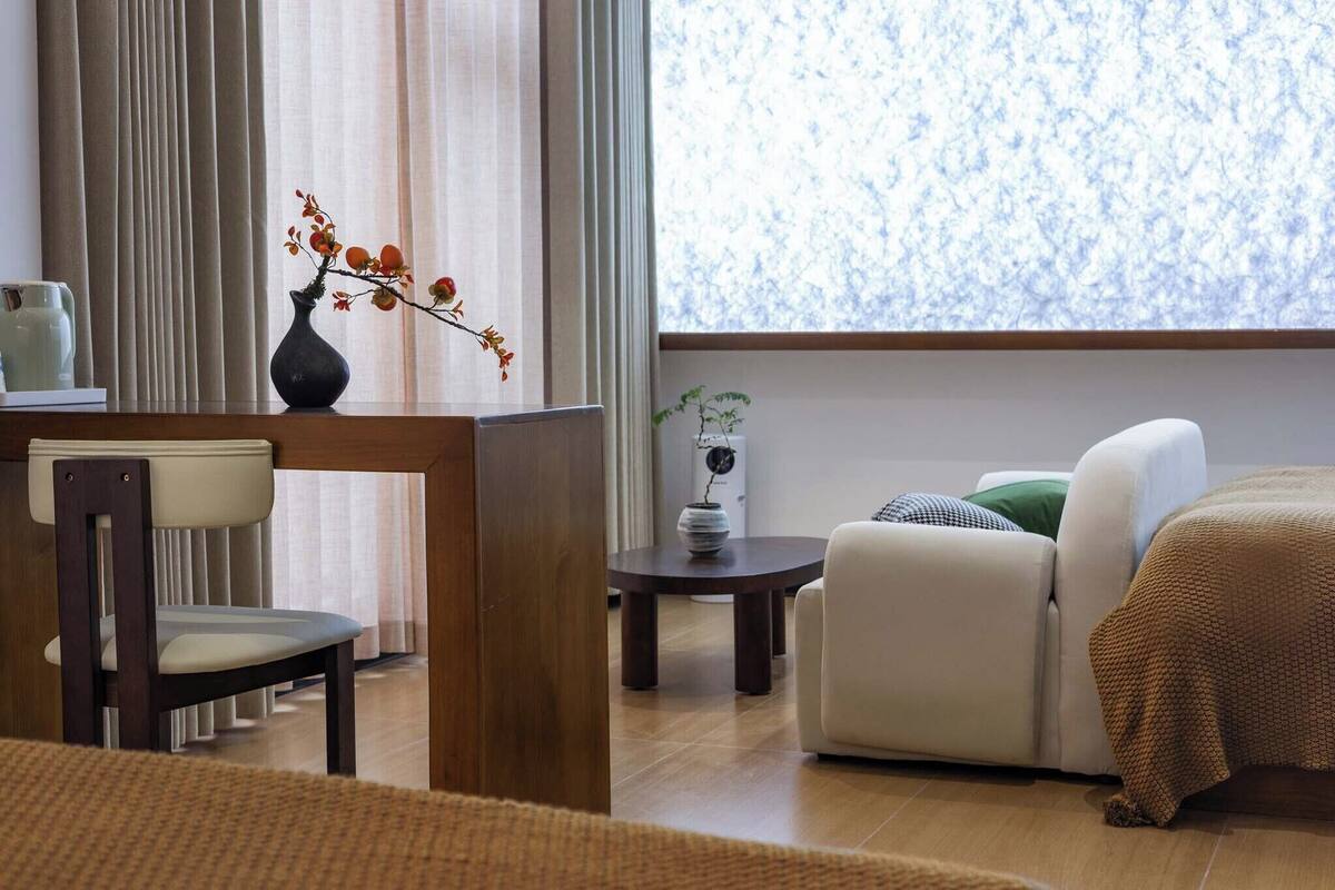 Een moderne woonkamer met een bank, een eettafel met stoelen, een vaas met bloemen en uitzicht op het groen door een raam.