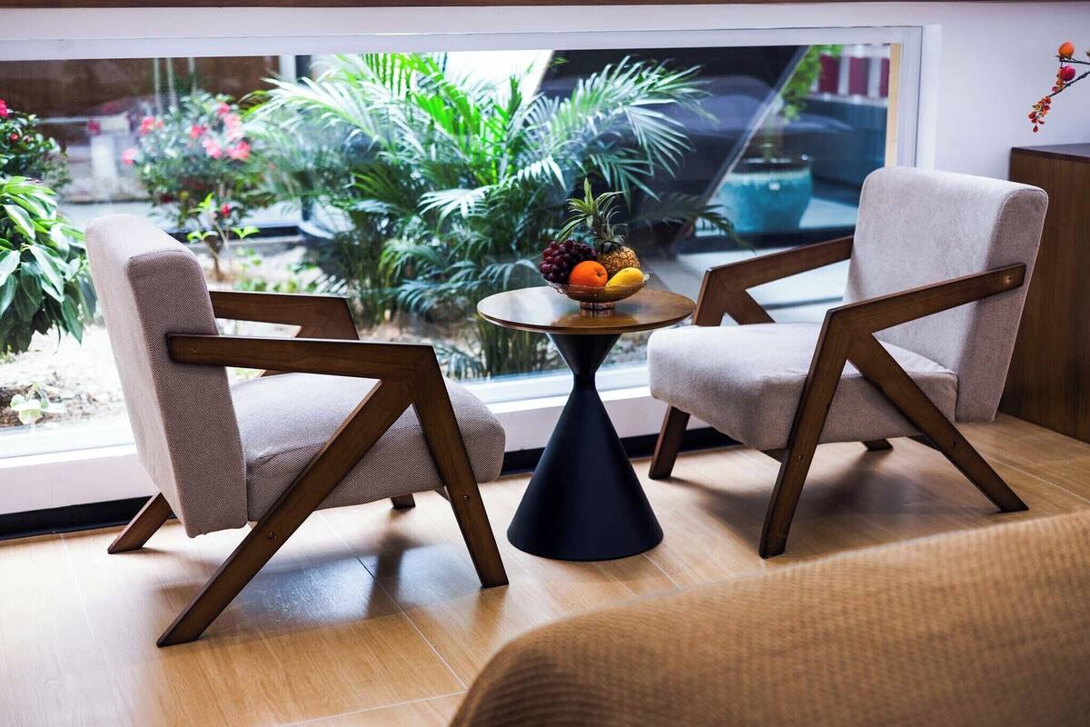 Een moderne kamer met twee stoelen, een ronde tafel met fruit en uitzicht op groen.