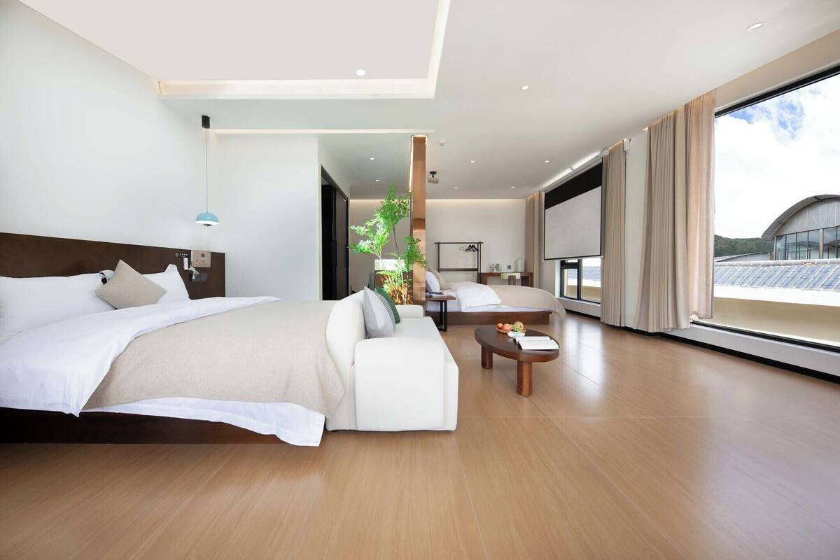 Een moderne hotelkamer met een groot bed, een slaapbank, een tafeltje en een groot raam met uitzicht.