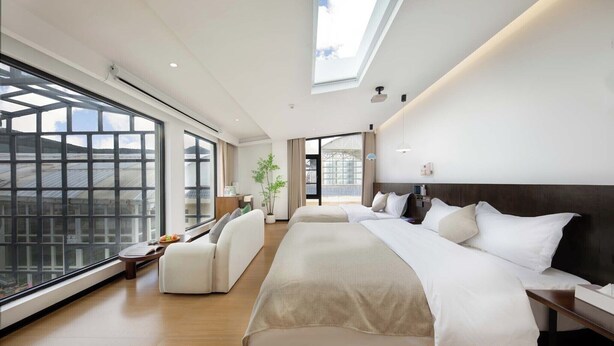 Une chambre d’hôtel moderne, dotée d’un grand lit, d’un canapé et offrant une vue sur la ville grâce à de grandes fenêtres.