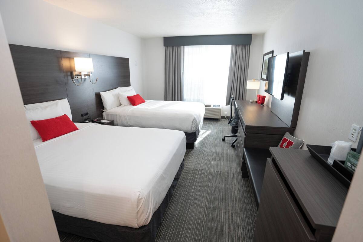 Hotelkamer met twee bedden, een bureau, een stoel, een televisie en een raam met gordijnen.