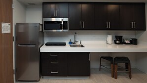 Une cuisine moderne avec des meubles de couleur sombre, des appareils en acier inoxydable et un plan de travail blanc.