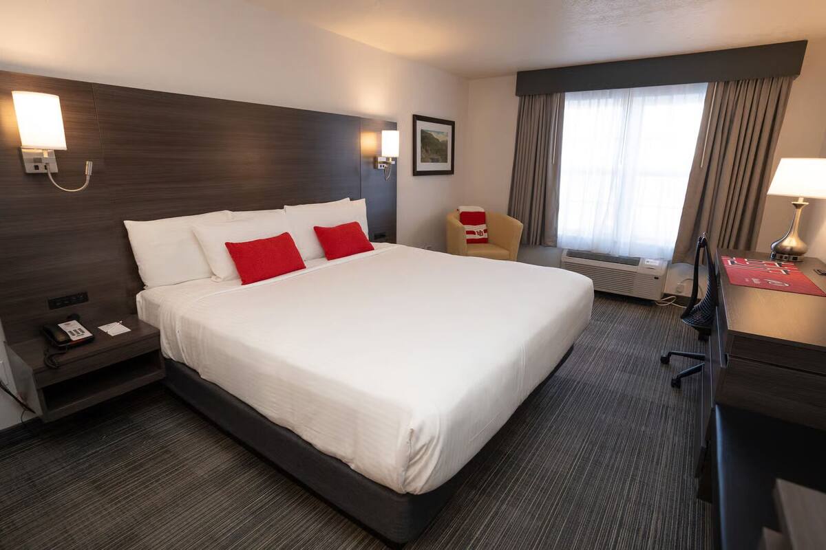 Hotelkamer met een groot bed, een bureau met lamp, een stoel, een telefoon en een schilderij aan de muur.
