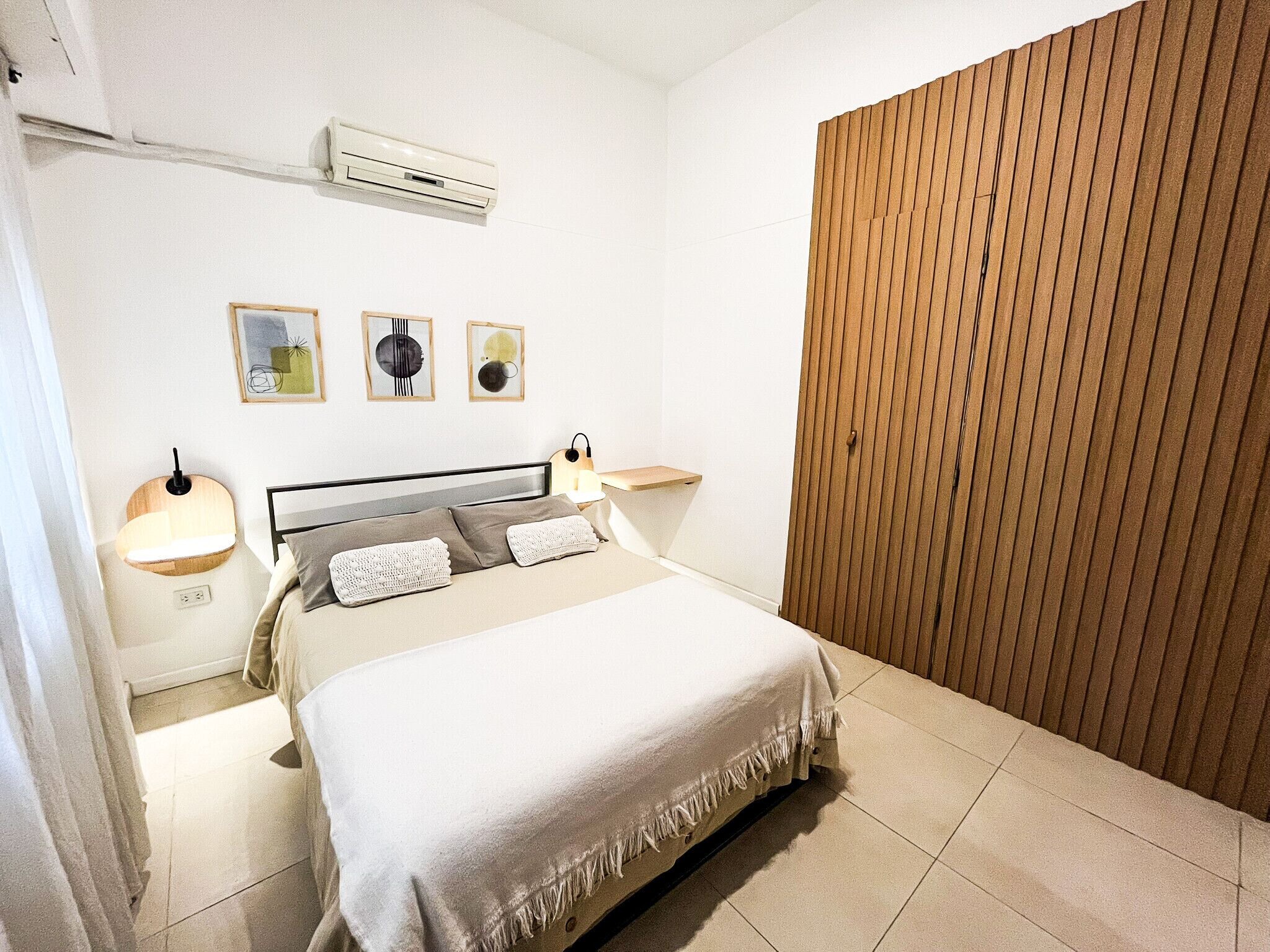 Un dormitorio con cama, lámparas de noche, aire acondicionado y un panel de pared de madera.