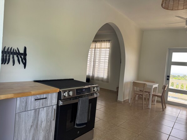 A kitchen with a stove, oven, and a dining area with a table and chairs. - 3-bedroom ocean-view house in peaceful Isabela with AC (Isabela)