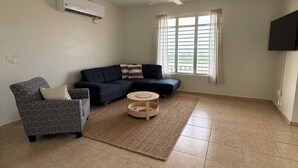 Uma sala de estar ampla com uma grande janela, um ventilador de teto e uma TV de tela plana na parede.