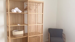 Um guarda-roupa de madeira com várias prateleiras e uma cesta, uma cadeira de vime e um tapete tecido em um quarto com piso de azulejos.