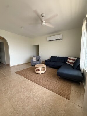 A living room with a dark blue sofa, a round wooden coffee table, a patterned armchair, and a ceiling fan.