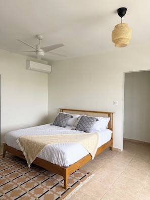 A bedroom with a wooden bed, white bedding, a patterned rug, a ceiling fan, and a woven light fixture. - 3-bedroom ocean-view house in peaceful Isabela with AC (Isabela)