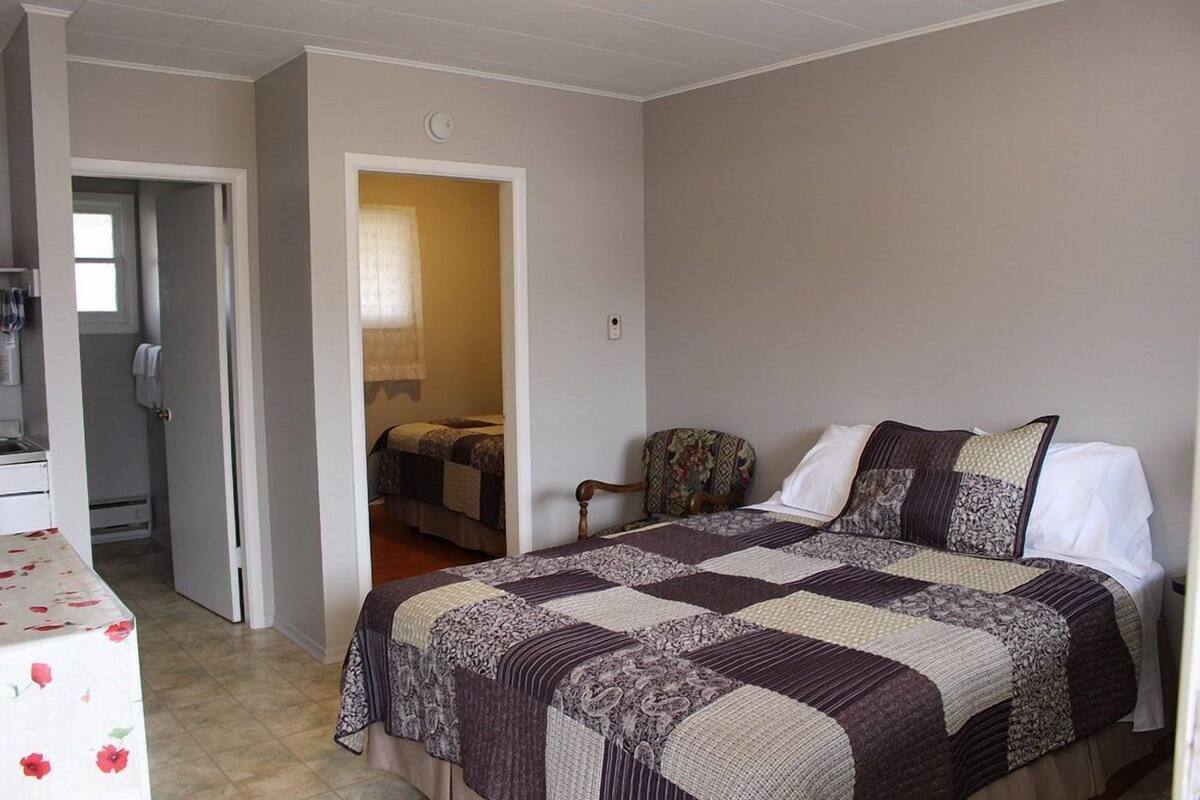 Ein Schlafzimmer mit einem großen Bett, einem Sessel und einem kleinen Tisch. Eine Tür führt in einen anderen Raum.
