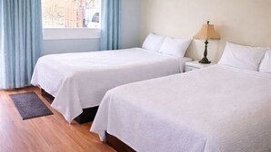 A hotel room with two beds, a nightstand with a lamp, a window with curtains, and a wooden floor. - THE VICTORIAN MOTEL AND RV PARK by Capital O (Grand Forks)