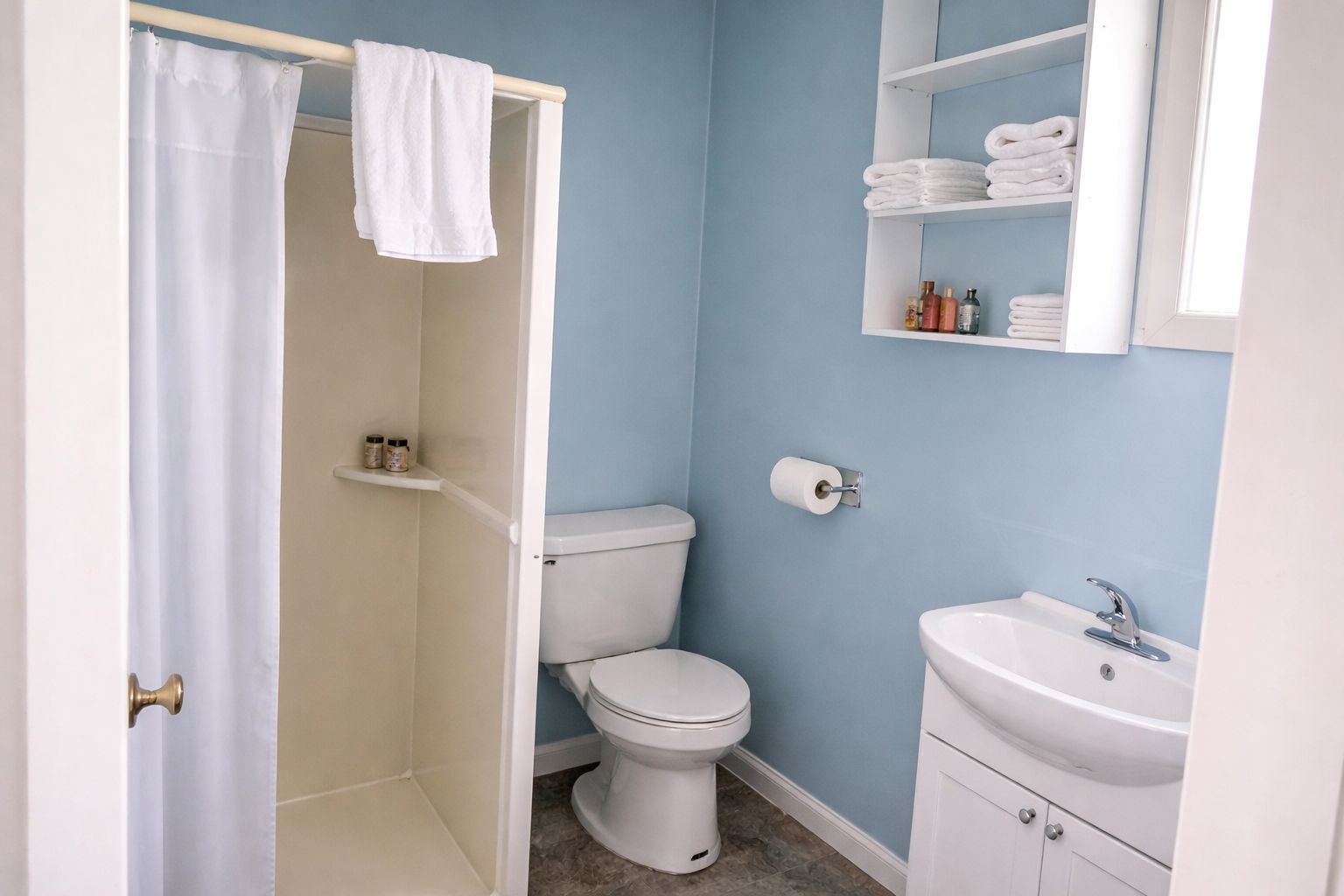 Et badeværelse med brusebad, toilet, håndvask og plads til håndklæder.