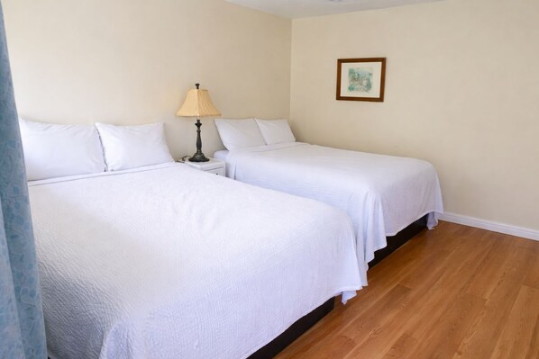 A room with two single beds, a nightstand with a lamp, a framed picture on the wall, and wooden flooring. - THE VICTORIAN MOTEL AND RV PARK by Capital O (Grand Forks)