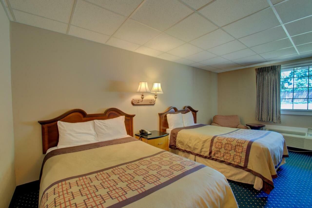 A hotel room with two beds, a nightstand, a lamp, and a window with curtains.