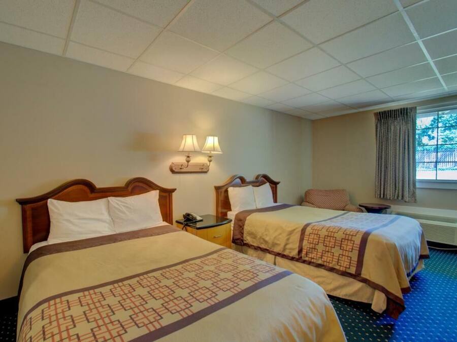 Une chambre d’hôtel avec deux lits, une table de chevet, une lampe et une fenêtre avec des rideaux.
