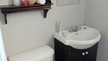 Een kleine badkamer met een wit toilet, een donker houten kastje met een wastafel, en een plank boven het toilet met toiletartikelen.
