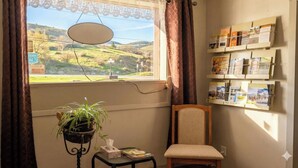 A room with a window view of a green landscape, a small table with a plant, a chair, and a wall-mounted bulletin board with pamphlets. - THE VICTORIAN MOTEL AND RV PARK by Capital O (Grand Forks)