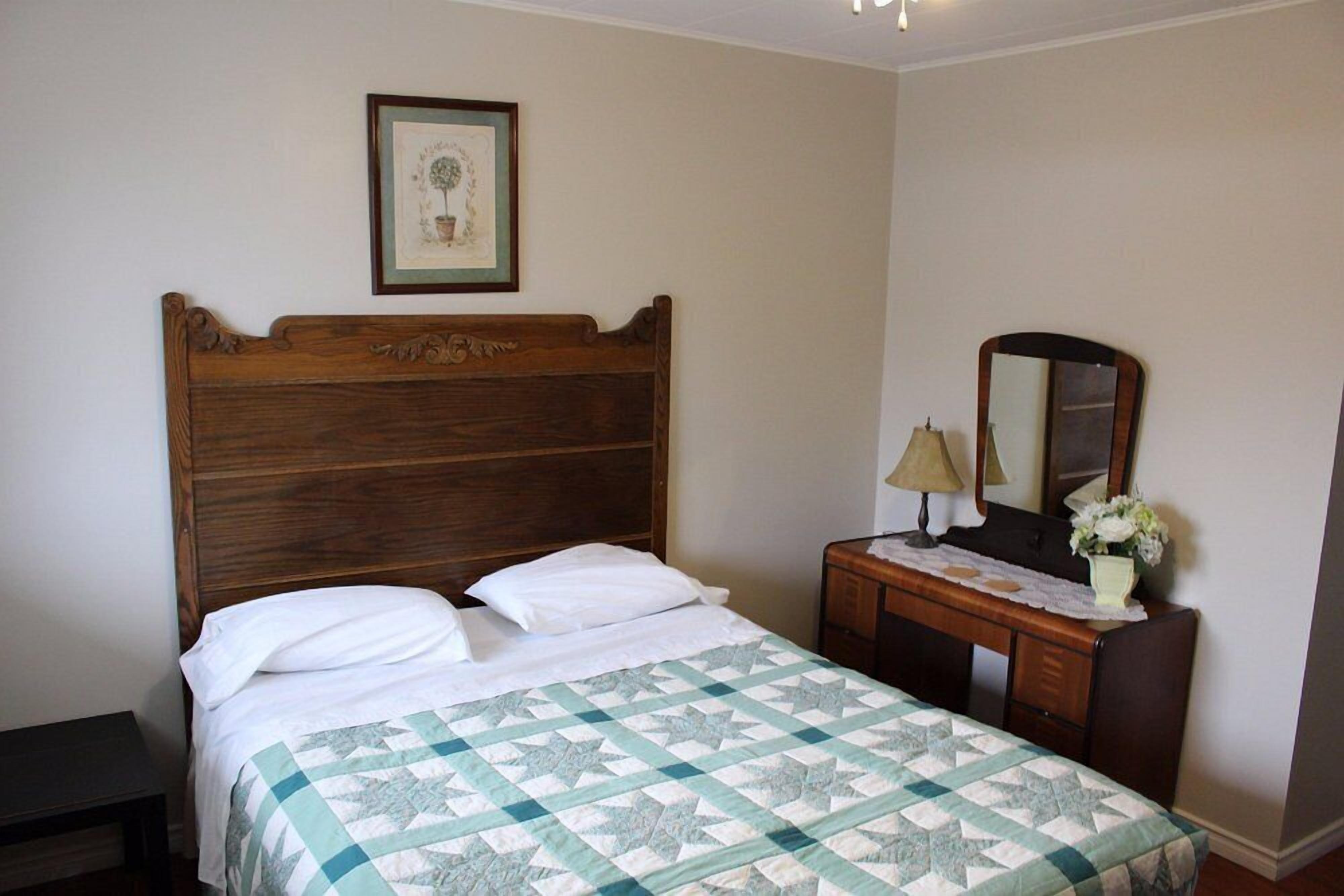 Um quarto com cama de madeira, uma mesa de cabeceira com abajur, um espelho e um quadro na parede.