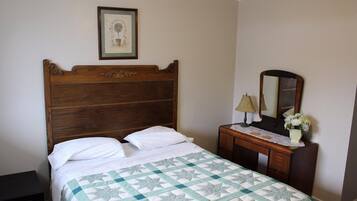 Um quarto com cama de madeira, uma mesa de cabeceira com abajur, um espelho e um quadro na parede.