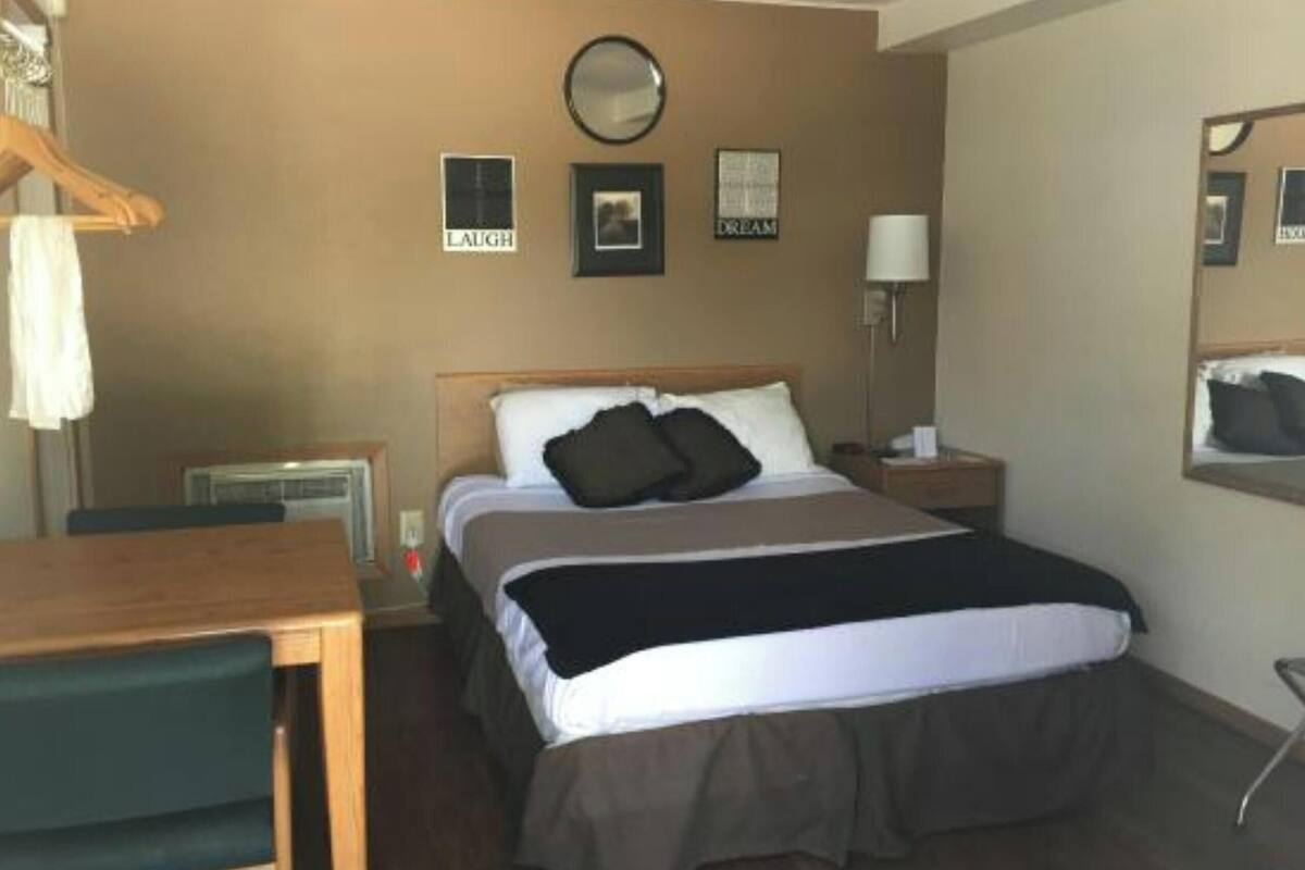 Ein Hotelzimmer mit Bett, Nachttisch, Lampe und Wanddekorationen, darunter ein Spiegel und gerahmte Bilder.