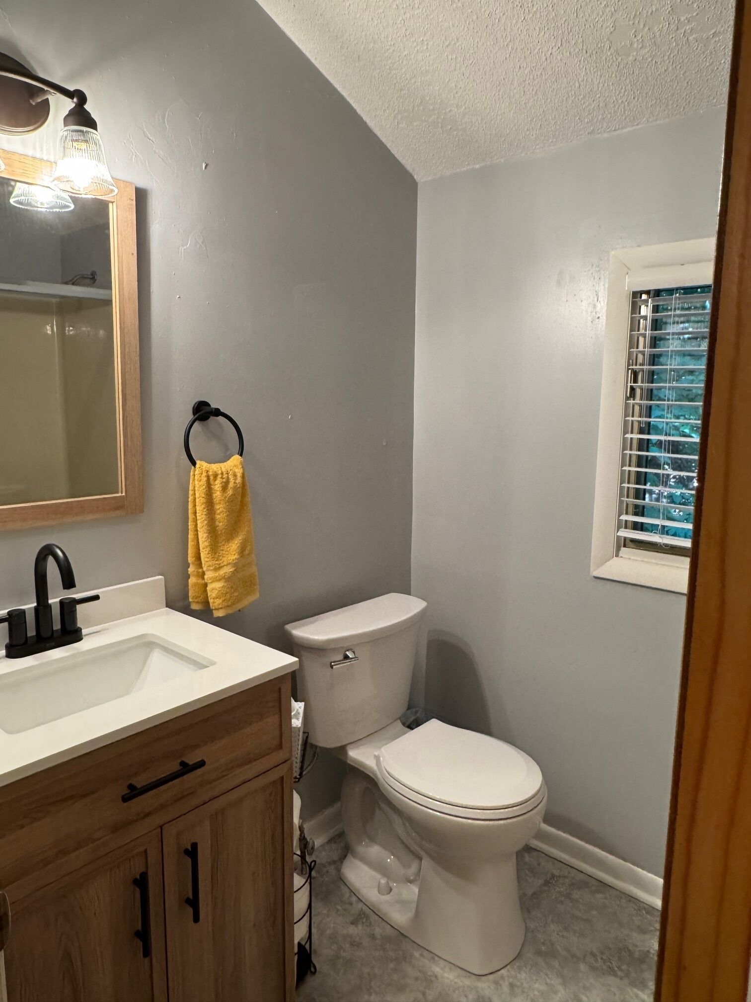 A bathroom with a white sink, wooden vanity, a toilet, and a mirror with lights.