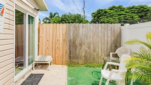 A small patio area with a wooden fence, a bench, and two white plastic chairs. - Pet-Friendly • Outdoor Space + Parking (Cape Coral)