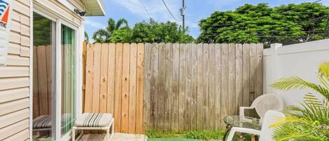 A small patio area with a wooden fence, a bench, and two white plastic chairs.