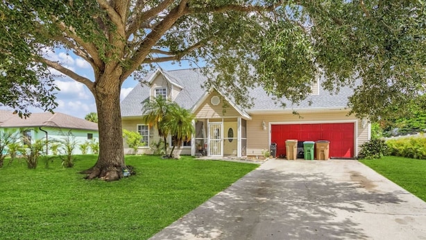 A two-story house with a red garage door, a large tree in the front yard, and a well-maintained lawn. - Pet-Friendly • Outdoor Space + Parking (Cape Coral)