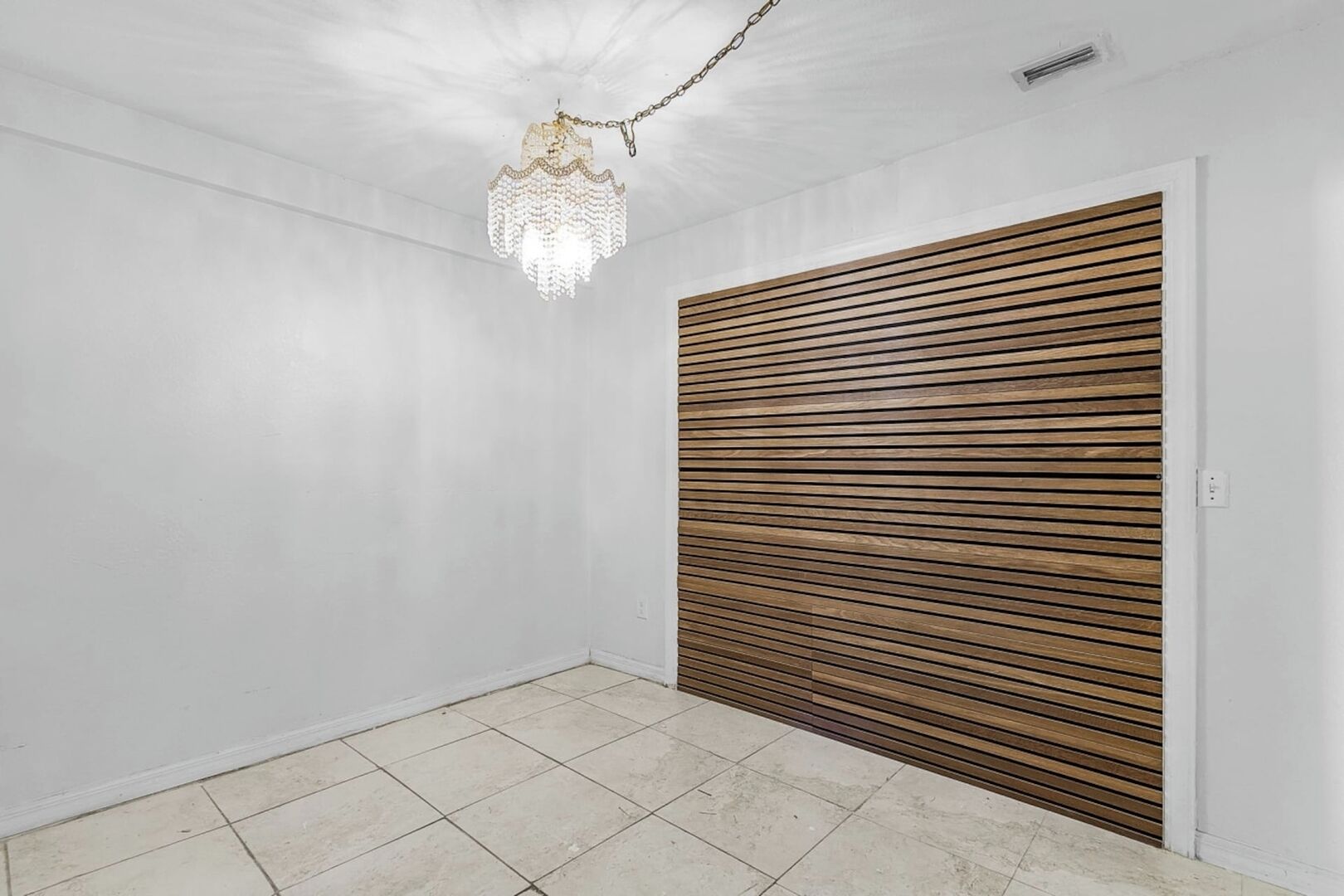 Ein Zimmer mit weiß gefliestem Boden, einer Holzschiebetür und einer hängenden Chandelier.