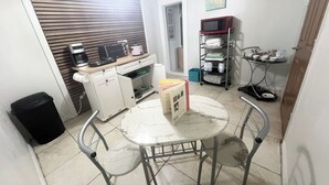 A compact kitchen with a microwave, toaster, and a small refrigerator. There is a dining table with chairs, a trash bin, and a metal shelf with dishes. - Pet-Friendly • Outdoor Space + Parking (Cape Coral)