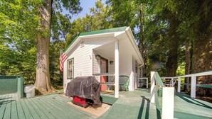 A wooden deck with a covered grill, a porch with a green roof, and a white house with a red door. - Earth's River Retreat: Kayaks, Wineries and GOTL (Austinburg Township)