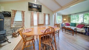 A cozy living room with a wooden dining table, chairs, a fireplace, a TV, and a sofa with cushions. - Earth's River Retreat: Kayaks, Wineries and GOTL (Austinburg Township)