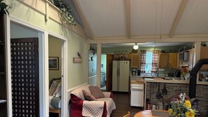 A cozy living room with a sofa, a dining table with a vase of flowers, and a kitchen in the background. - Earth's River Retreat: Kayaks, Wineries and GOTL (Austinburg Township)