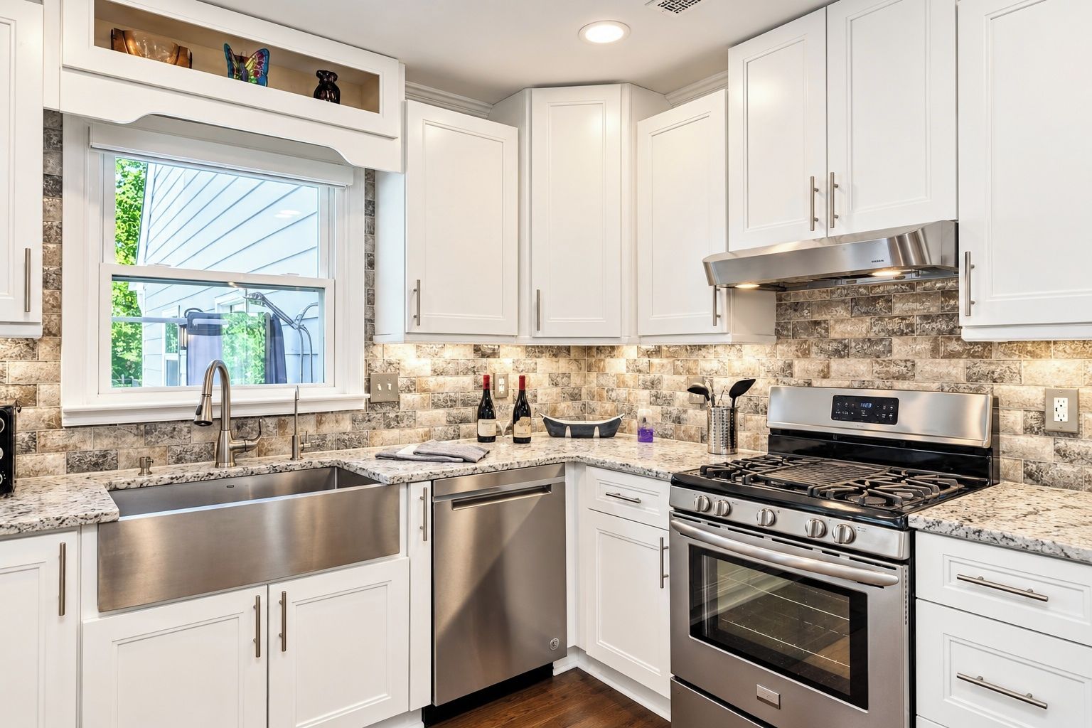 A modern kitchen with white cabinets, stainless steel appliances, and a window with a view of greenery.