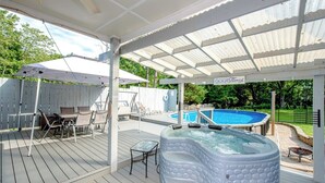 A covered outdoor deck with a hot tub, pool, and seating area. - CLT Oasis (Charlotte)
