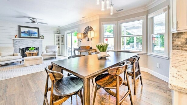A spacious dining area with a large wooden table and chairs, a fireplace, and large windows offering views of the outdoors. - CLT Oasis (Charlotte)