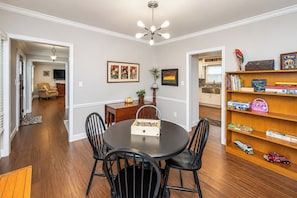 A dining area with a round table, chairs, a bookshelf with toys, and a painting on the wall.