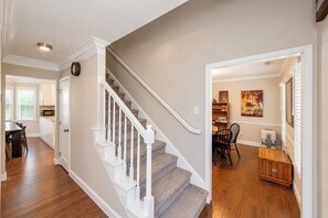 A staircase with white balusters leading to a landing, a dining area with a table and chairs, and a kitchen area with a microwave.
