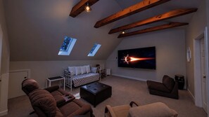 A cozy living room with a sofa, ottoman, and chairs, a flat-screen TV, and skylights.