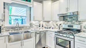 A modern kitchen with white cabinets, a stainless steel sink, a gas stove, and a dishwasher. - CLT Oasis (Charlotte)