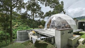 Estructura en forma de geodésica con una plataforma de concreto, una hamaca y un pequeño rincón de estar.