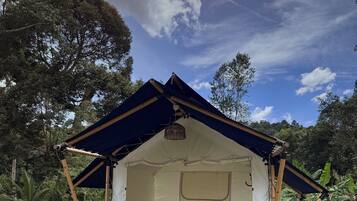 A tent with a flat roof, a small table, and a bench in a grassy area.