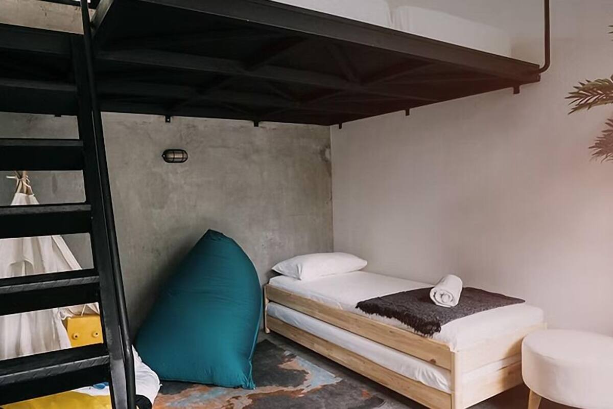 Een kleine kamer met een stapelbed, een enkel bed en een zithoekje.