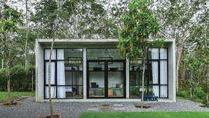 Un edificio moderno de una sola planta con amplios ventanales y puertas de vidrio, rodeado de un área boscosa y natural.