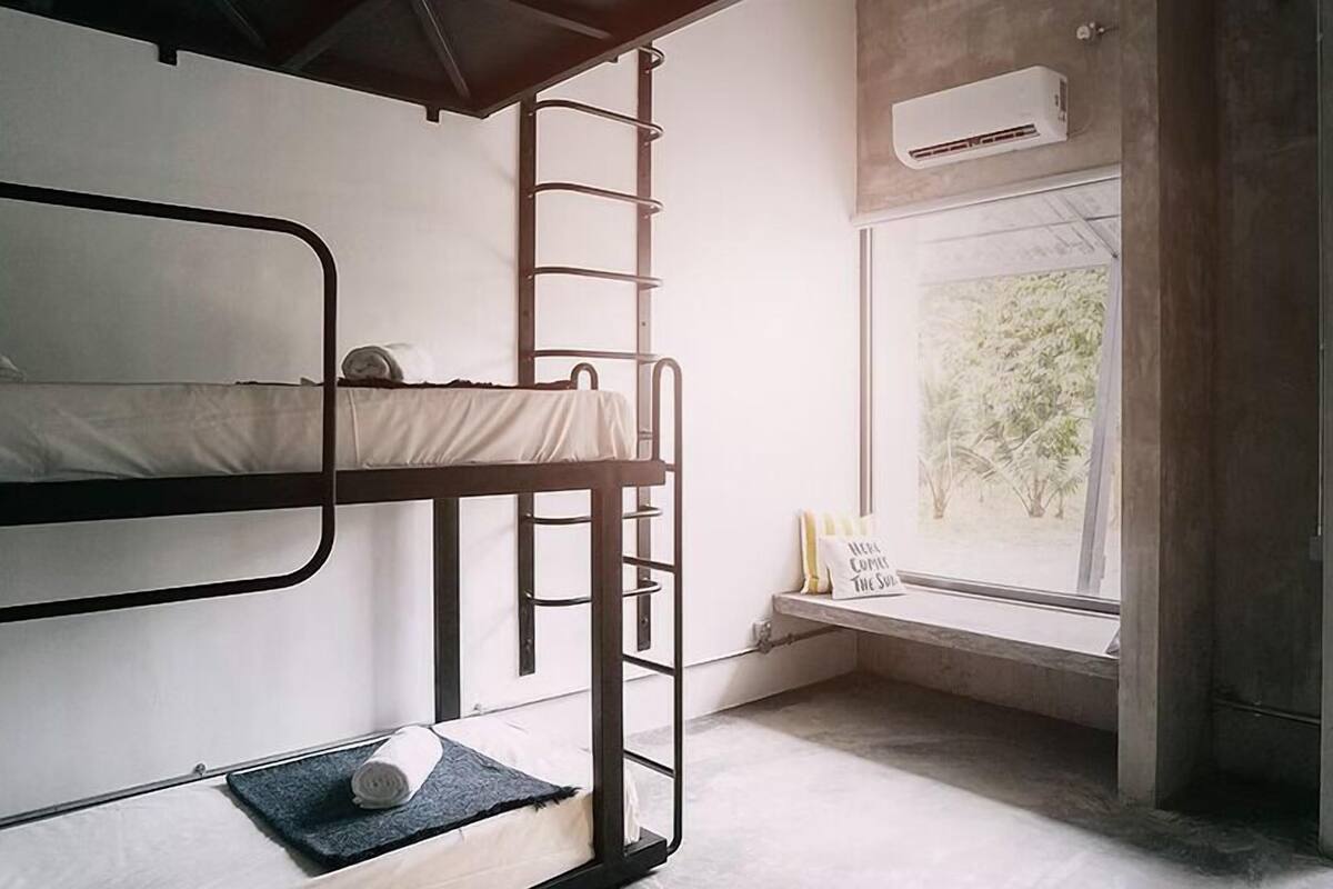 Een slaapkamer met een stapelbed, een raam met uitzicht op bomen, en een airconditioning.