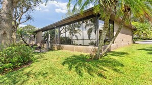 A modern building with large glass windows, a covered patio, and a well-maintained lawn with palm trees.