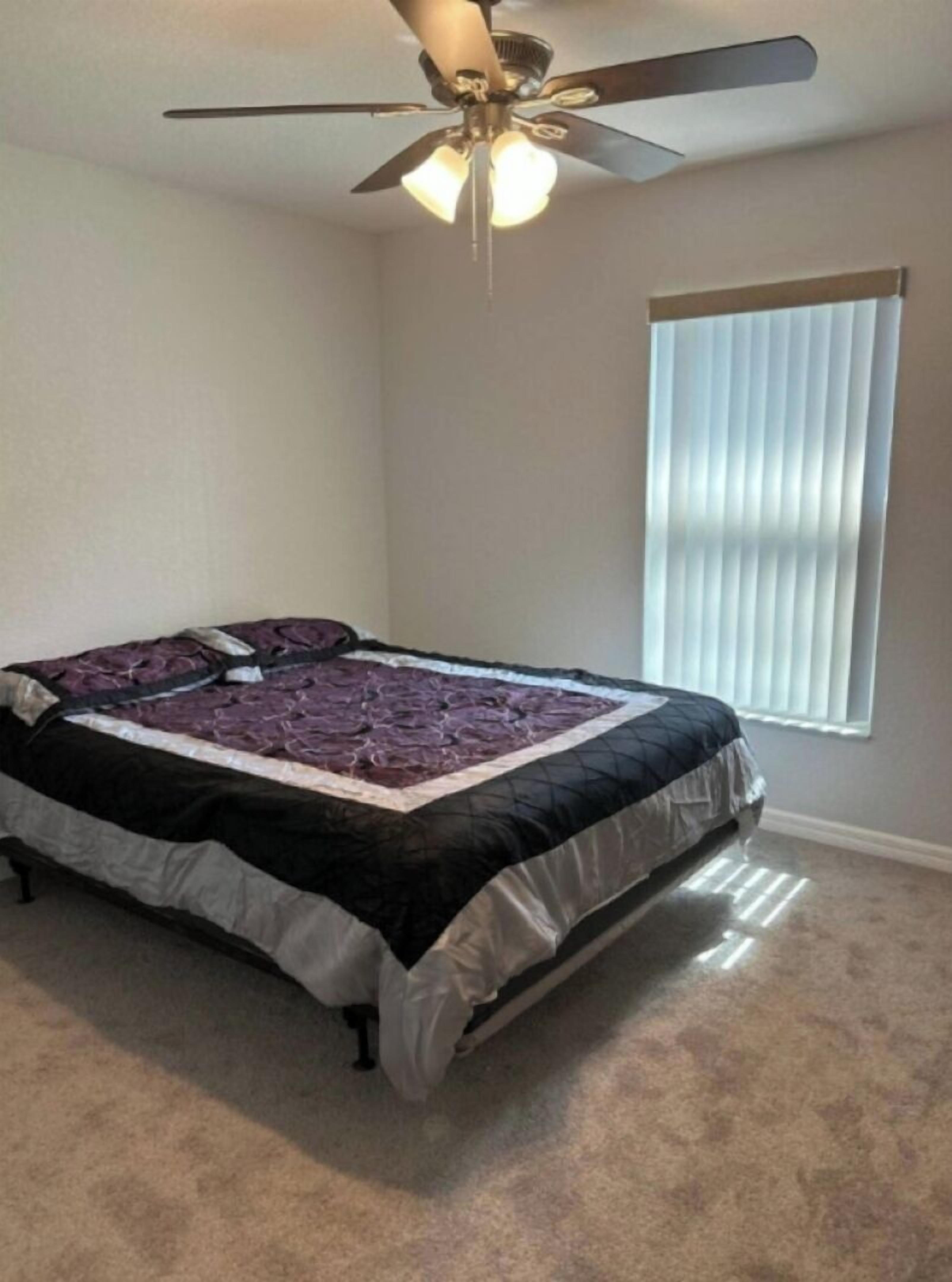 A bedroom with a bed, a ceiling fan, and a window with blinds.