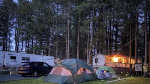 A campsite with multiple tents, a caravan, and a lit building in the background. - RV-accessible cozy private campground with pool access near Lake Wallenpaupack (Hawley)